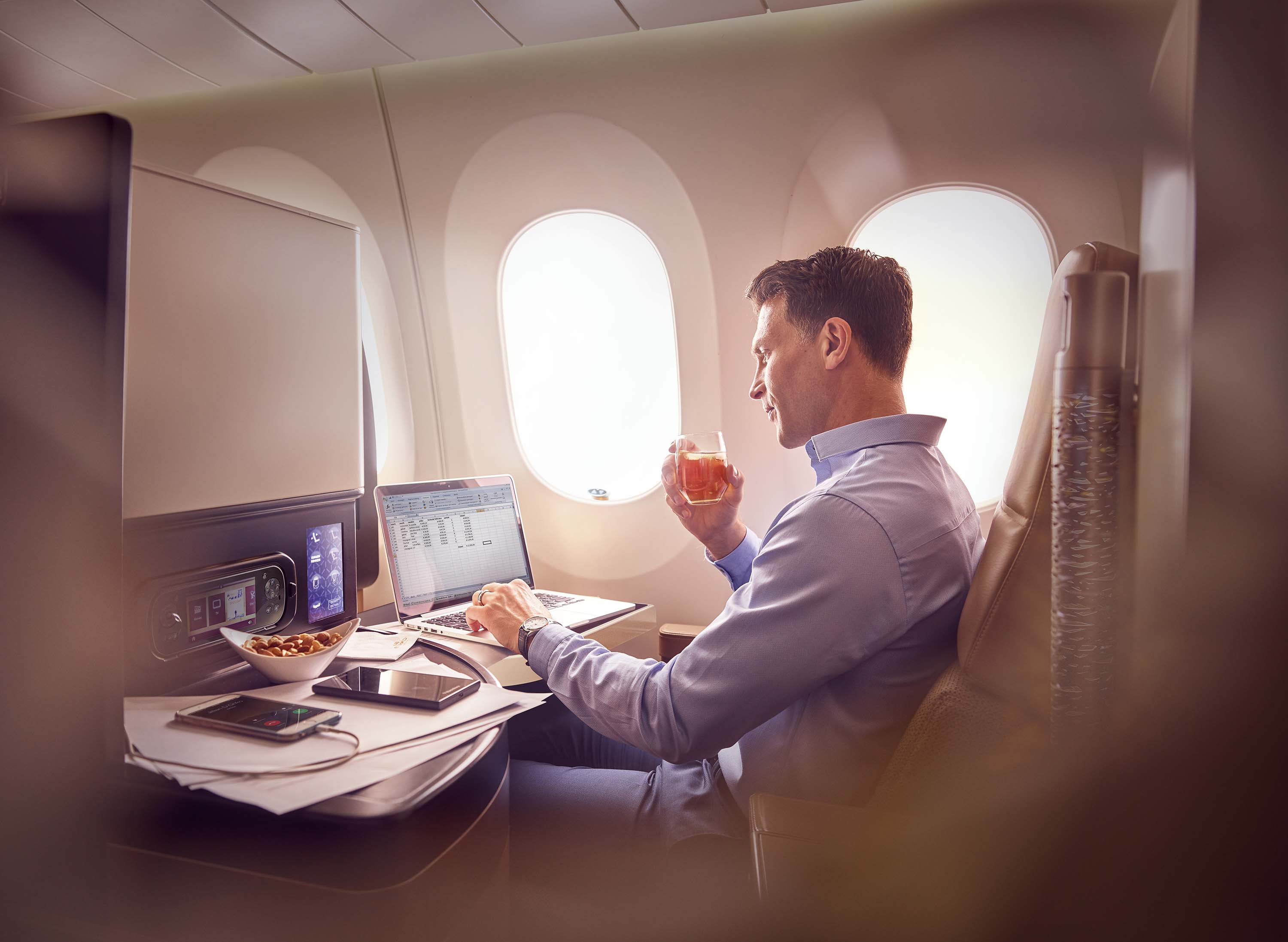 a man sitting in an airplane with a glass of liquid and a laptop