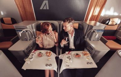 a man and woman sitting in a chair with food and drinks